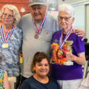 elderly residents pose wearing medals, around Dinora Negrete, the staff member who started the "walk to Kansas" challenge.