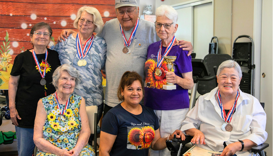 elderly residents pose wearing medals, around Dinora Negrete, the staff member who started the "walk to Kansas" challenge.
